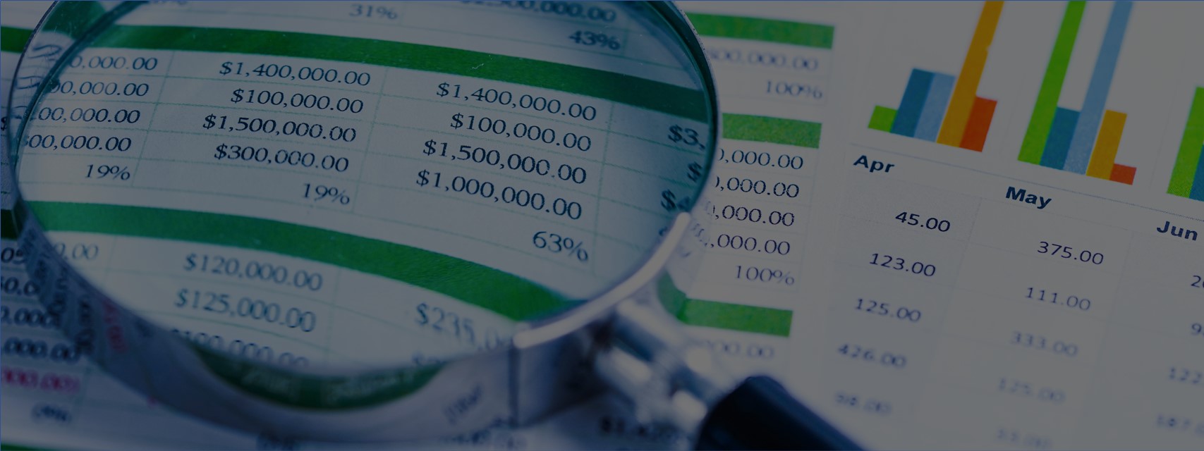 A magnifying glass placed over a printout of a spreadsheet showing dollar amounts and a chart of monthly figures.