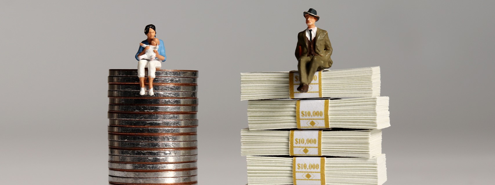 A woman with a baby sitting on a pile of coins and a man in a suit sitting on a pile of $10,000 packets of bills.