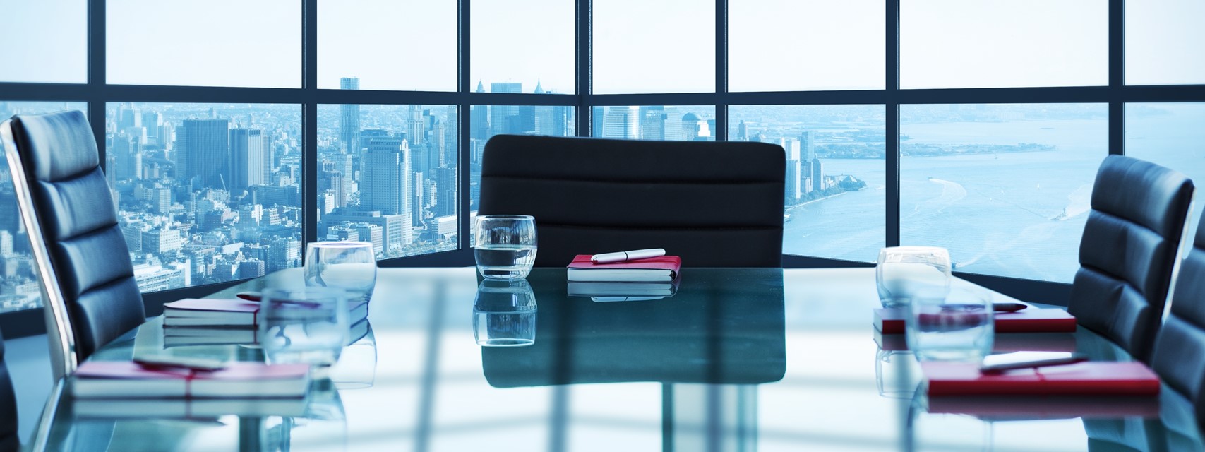 Image of a boardroom with NY cityscape seen in background through large window.