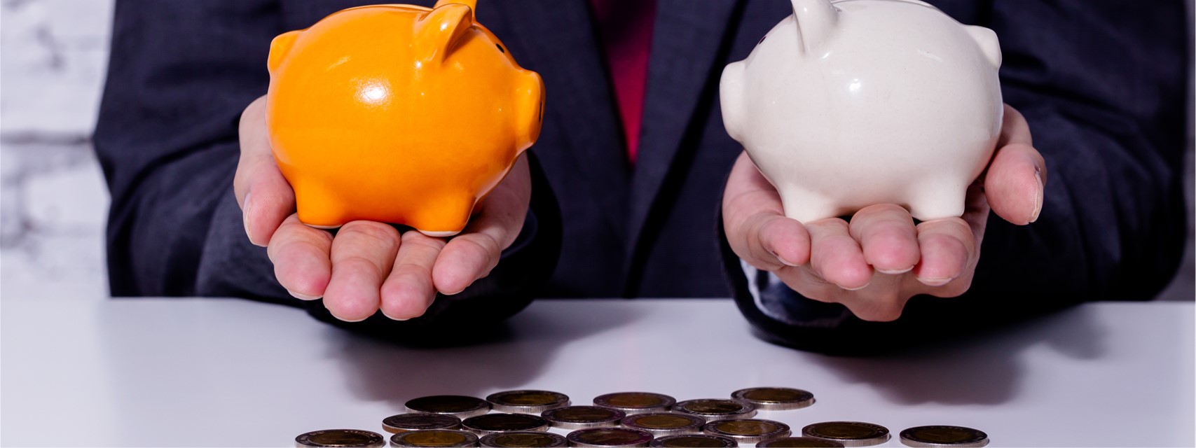 business man weighing two piggy banks above a pile of coins