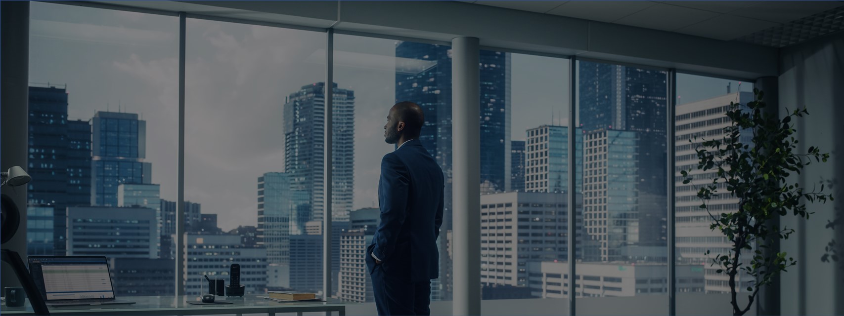 Black executive gazing thoughtfully out window from high floor of office building