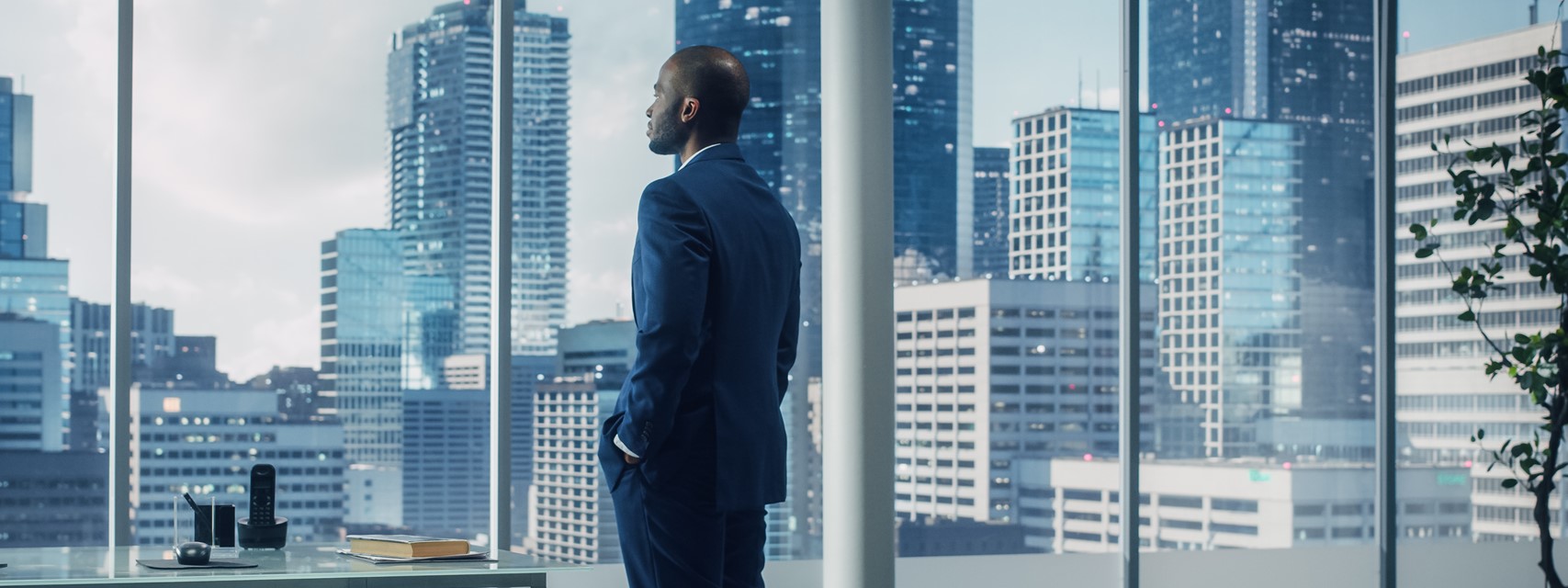 Black executive gazing thoughtfully out window from high floor of office building