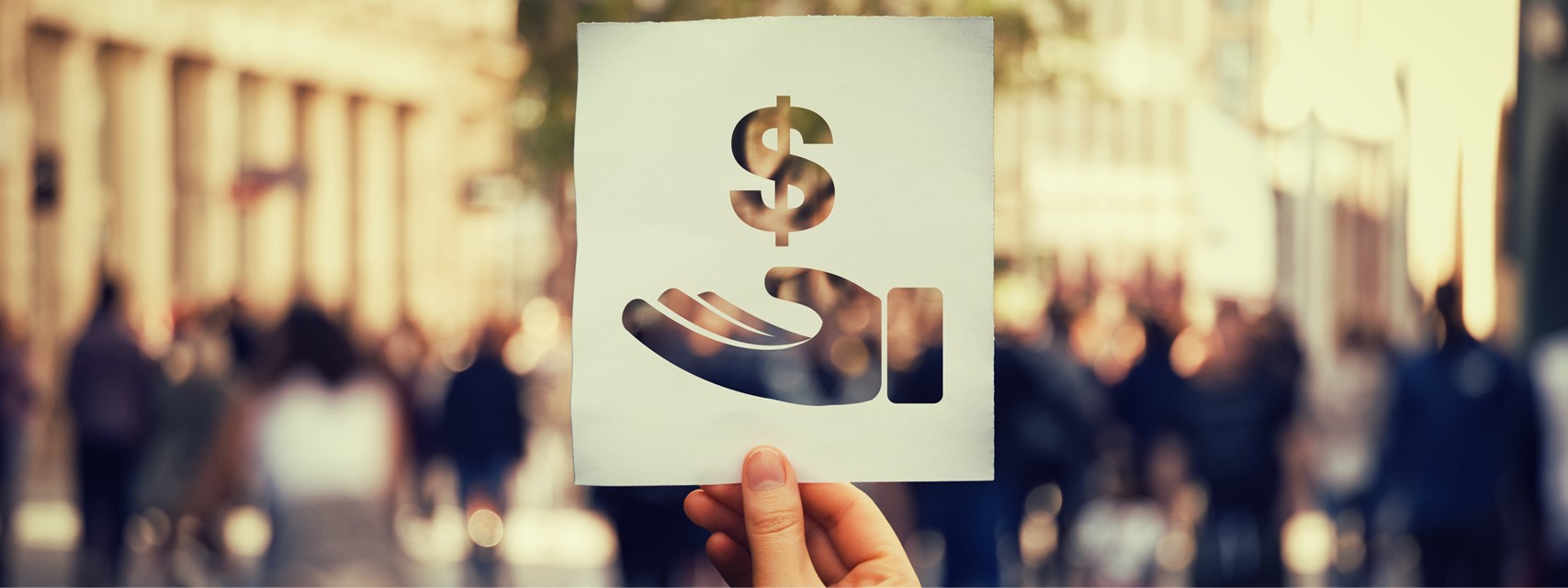 Paper with cut-out dollar sign held up in front of street with business people