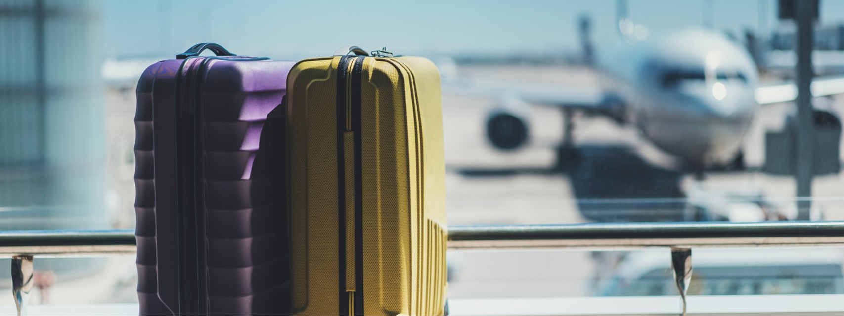 Two suitcases in the airport departure lounge, airplane in the background