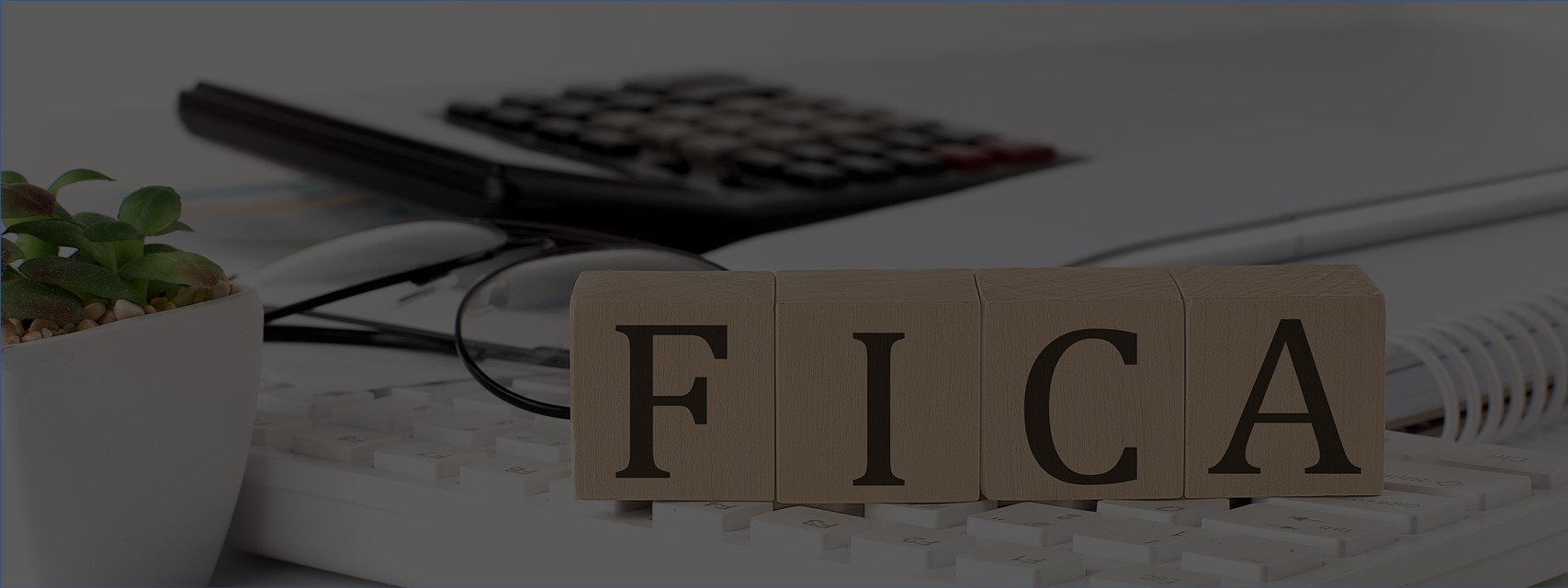 Wooden blocks spelling out "FICA" on computer keyboard with calculator in background