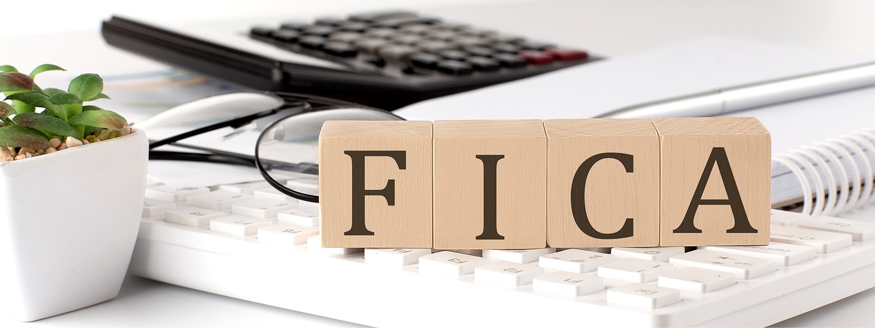 Wooden blocks spelling out "FICA" on computer keyboard with calculator in background