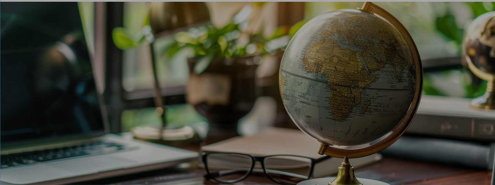 A desk with a laptop computer, books, eyeglasses, and a globe.
