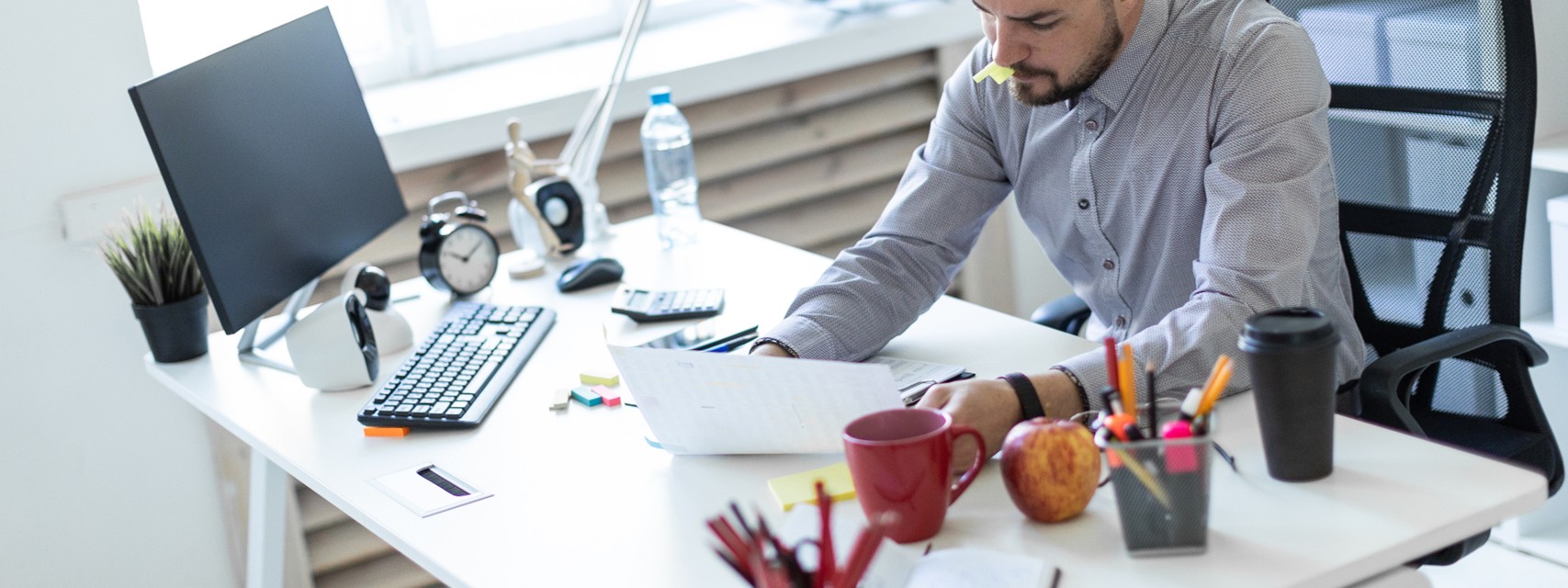 Investor reviewing a company's cap table - A young man in the office sits at a table, holds a cap from the marker in his mouth and works with documents.