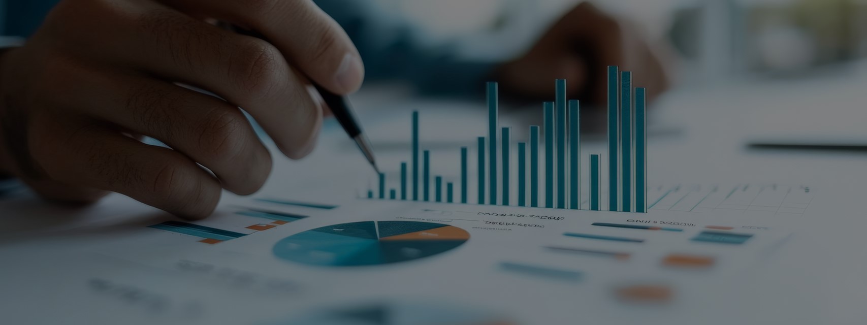 A close-up of a hand holding a pen, pointing at financial charts on paper, representing financial reporting and analysis.