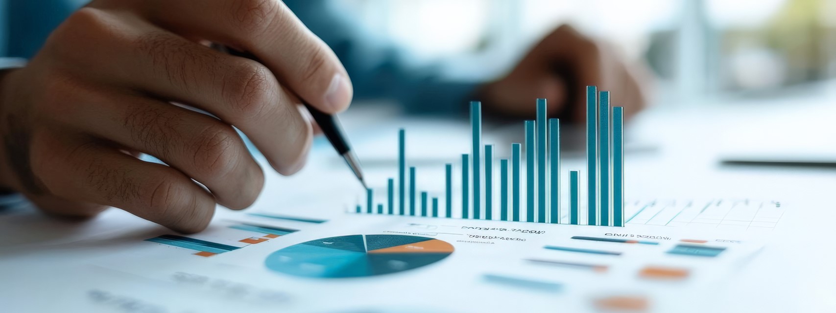 A close-up of a hand holding a pen, pointing at financial charts on paper, representing financial reporting and analysis.