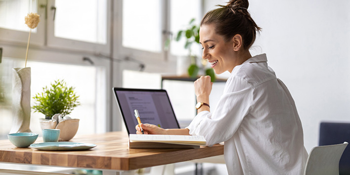 Woman taking notes while working on laptop
