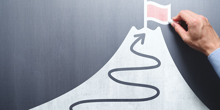 Businessman drawing waving path to the top of a mountain to reach a flag or goal